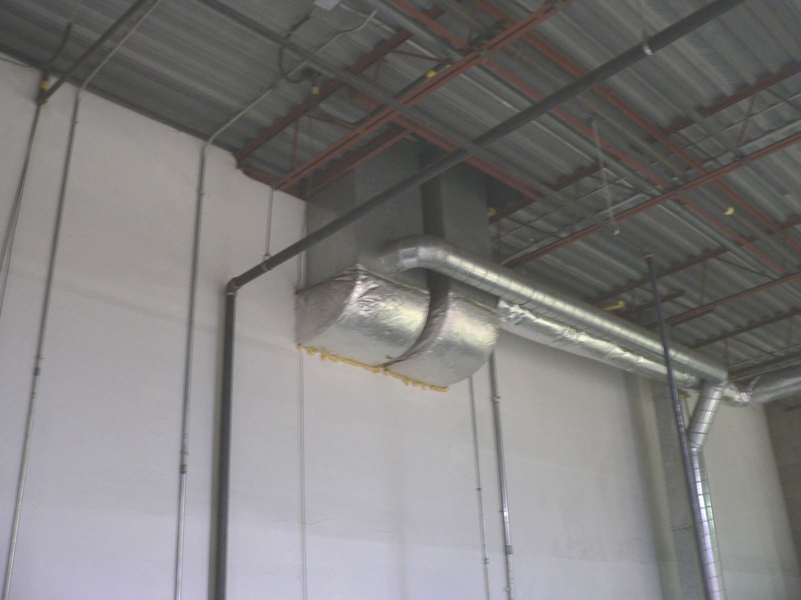 Metal and foil wrapped ducts running along a wall and ceiling