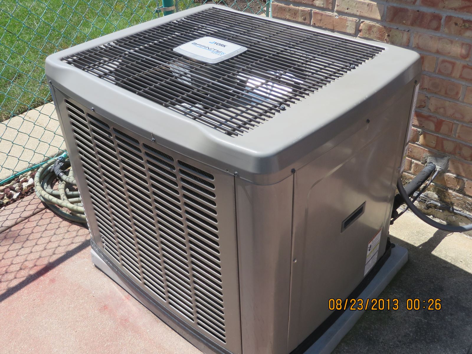 An outdoor condenser unit for a central air conditioner beside a brick house